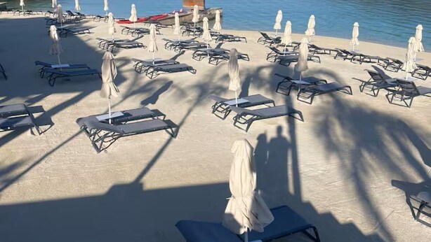 A beach with sun loungers and umbrellas, a lifeguard tower, and a calm sea.