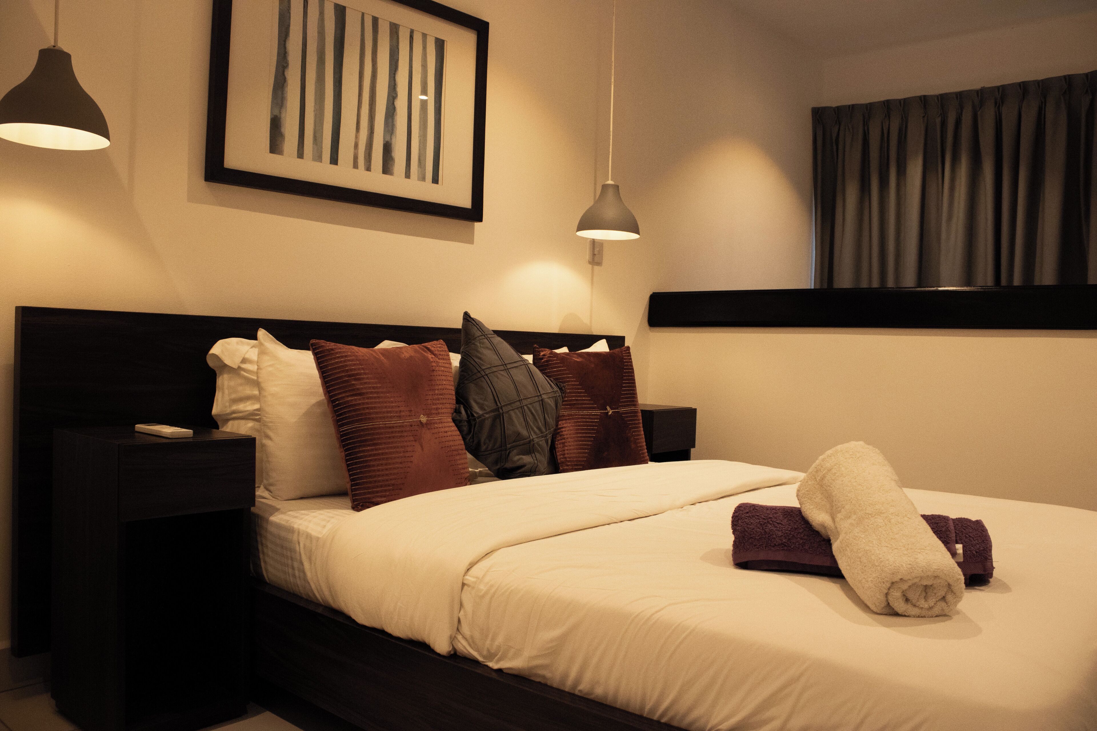 A neatly made bed with a rolled towel, dark headboard, and two bedside tables with lamps.