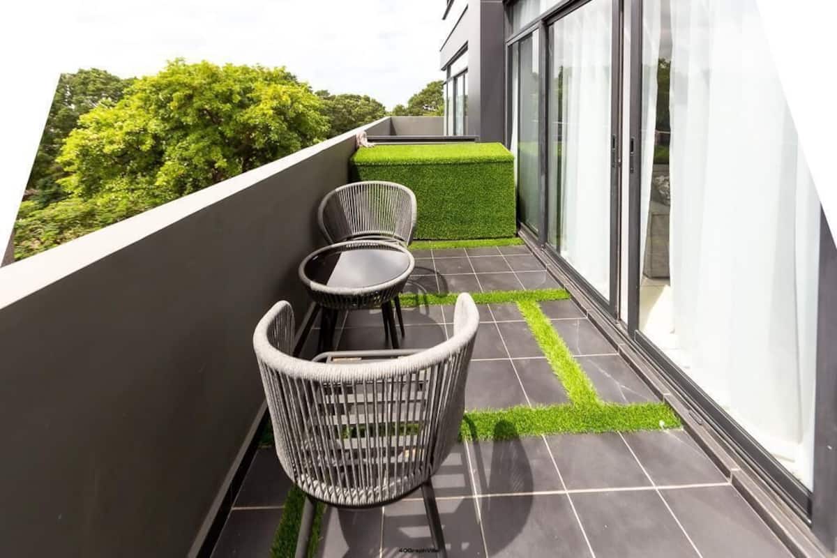 A balcony with two wicker chairs, a small table, and a neatly trimmed green hedge.