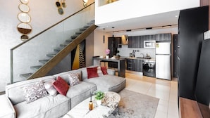 A modern apartment with a living area featuring a grey sectional sofa, a marble coffee table, and a staircase leading to an upper floor. - Premium Suite (Accra)