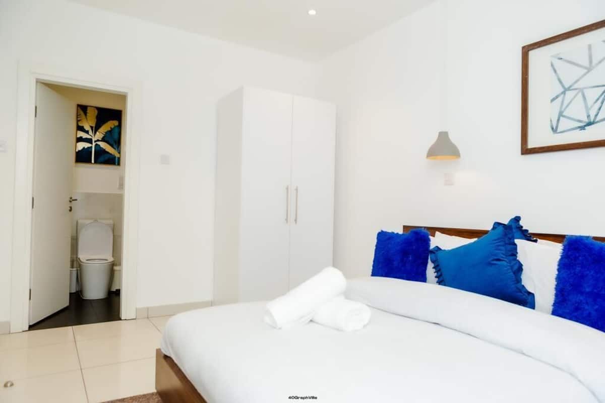 A bedroom with a bed, a wardrobe, a bathroom, and a wall-mounted lamp.