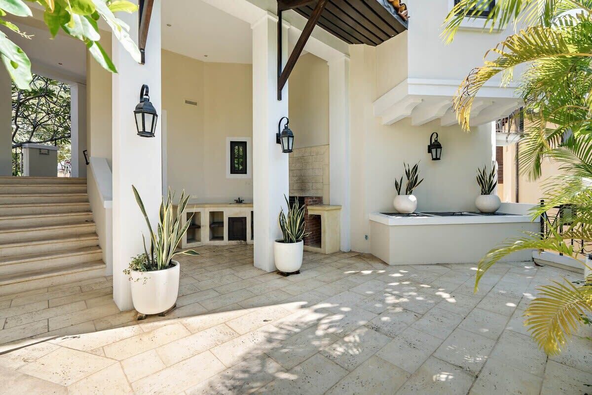 A covered outdoor area with potted plants, a stone floor, and wall-mounted lanterns.