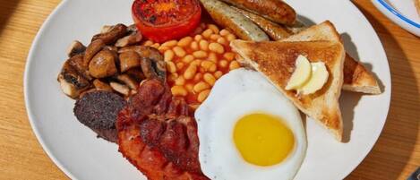 Un plato de comida para el desayuno con huevos, tocino, salchichas, frijoles, champiñones y tostadas.