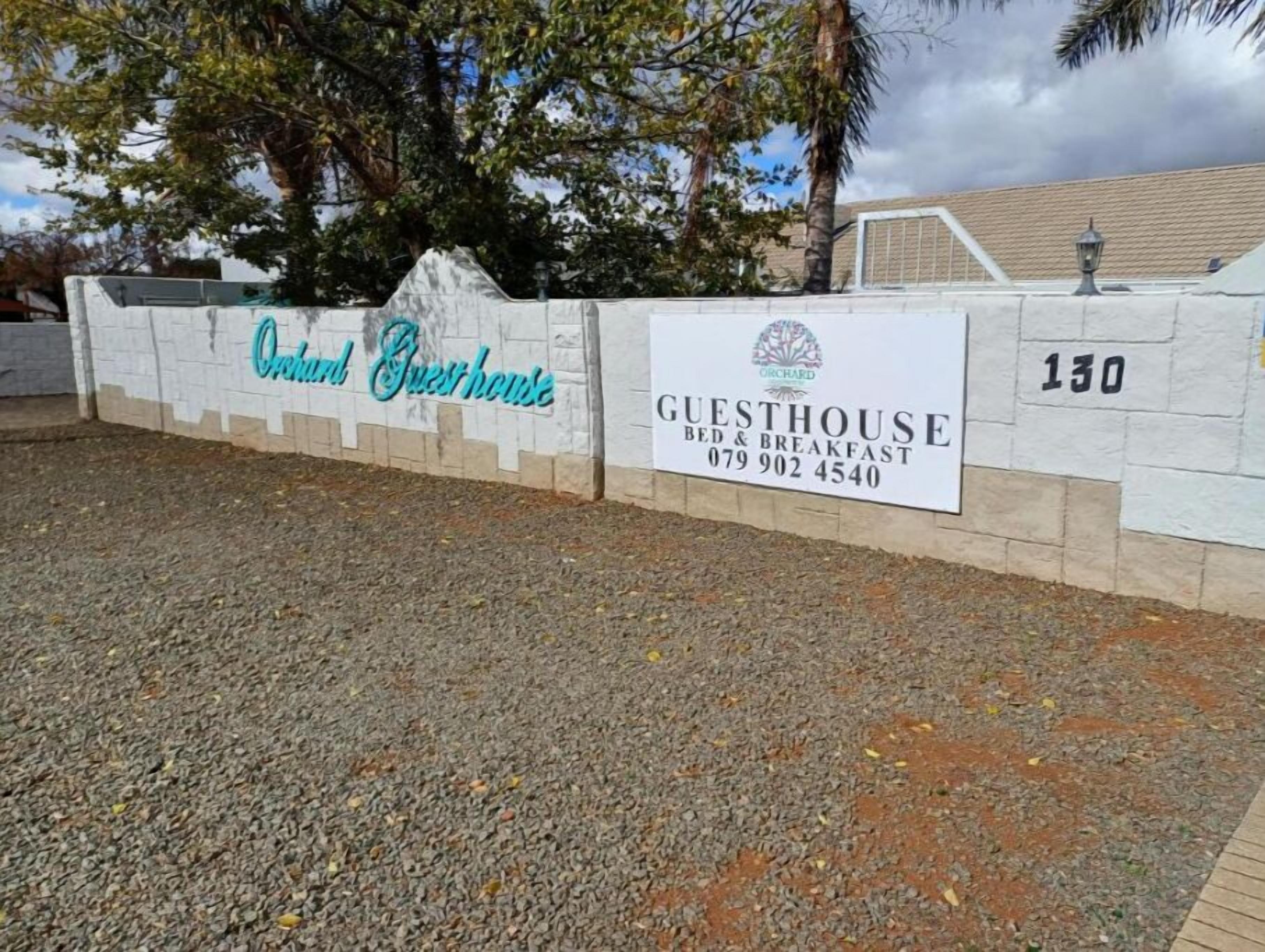 A sign for Orchard Guesthouse with contact information and a number 130.