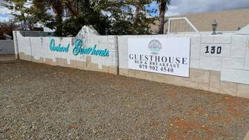A sign for Orchard Guesthouse with contact information and a number 130.