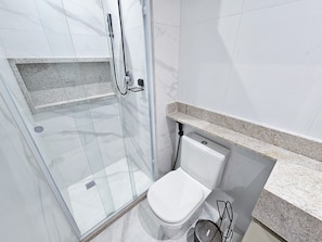 A modern bathroom with a glass-enclosed shower, a white toilet, and a granite countertop.