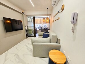 A modern living room with a flat-screen TV, a sofa, a coffee table, and a dining area visible through an open door. - Mirante de Porto - Porto de Galinhas (Ipojuca)