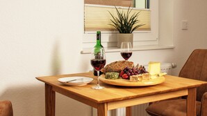 A wooden table with a plate, a glass of red wine, a bottle of wine, a cheese board with grapes and nuts, and a potted plant. - Idyllic vacation apartment 300m from the Zwischenahner Meer (Bad Zwischenahn)