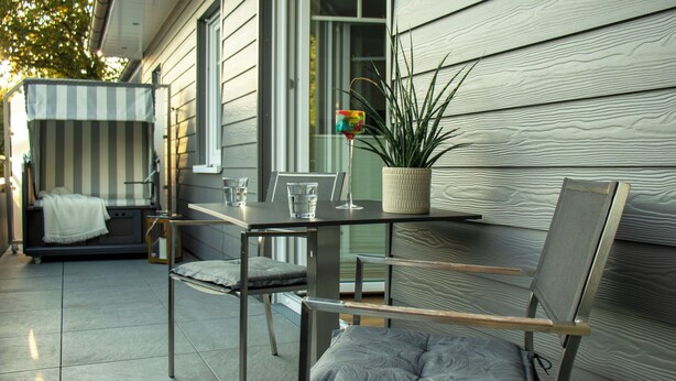 A patio with a table, two chairs, a small table with a plant, and a striped awning. - Idyllic vacation apartment 300m from the Zwischenahner Meer (Bad Zwischenahn)