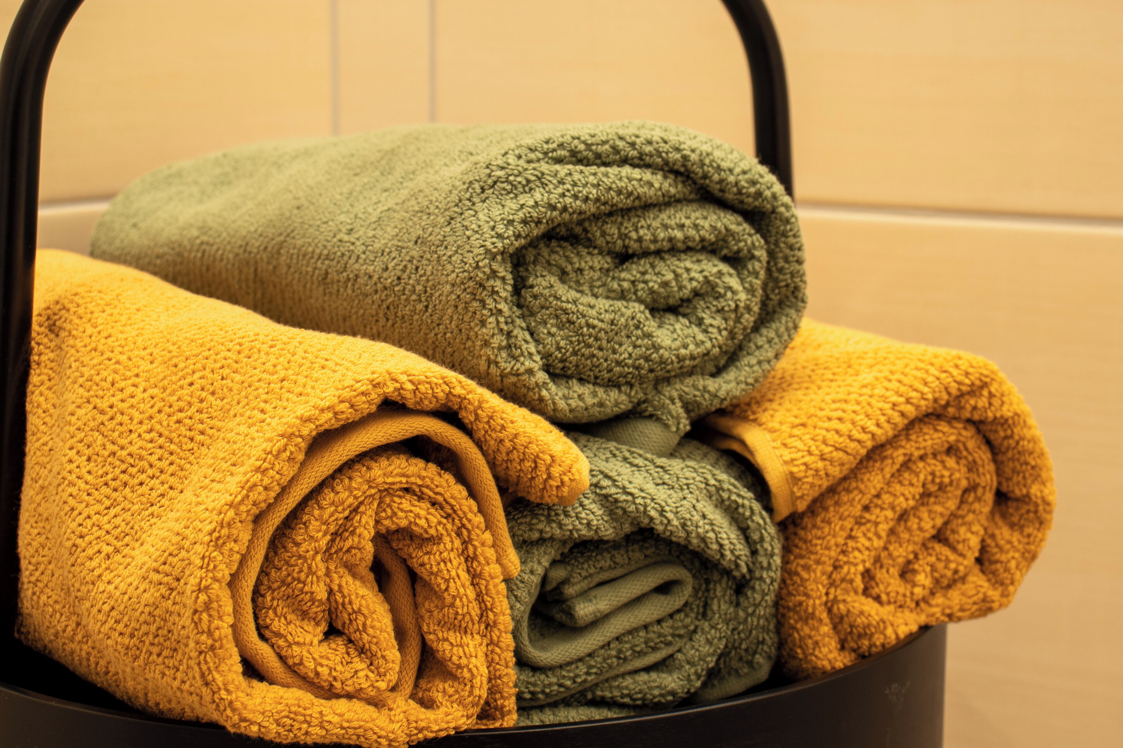 Uma cesta de metal preta com toalhas enroladas em tons de amarelo e verde.