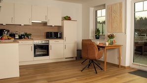 A modern kitchen with white cabinets, a built-in oven, and a dining area with a wooden table and a brown chair. - Idyllic vacation apartment 300m from the Zwischenahner Meer (Bad Zwischenahn)