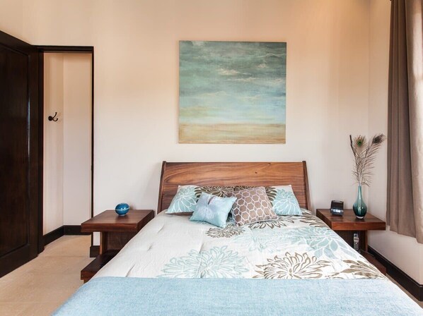 A bedroom with a wooden bed, a nightstand with a vase, and a painting on the wall. - Beautiful Mediterranean-Style Penthouse with an Oceanview Balcony (Las Catalinas)
