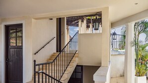 A multi-level house with a staircase, a dark door, and a balcony with potted plants. - Beautiful Mediterranean-Style Penthouse with an Oceanview Balcony (Las Catalinas)