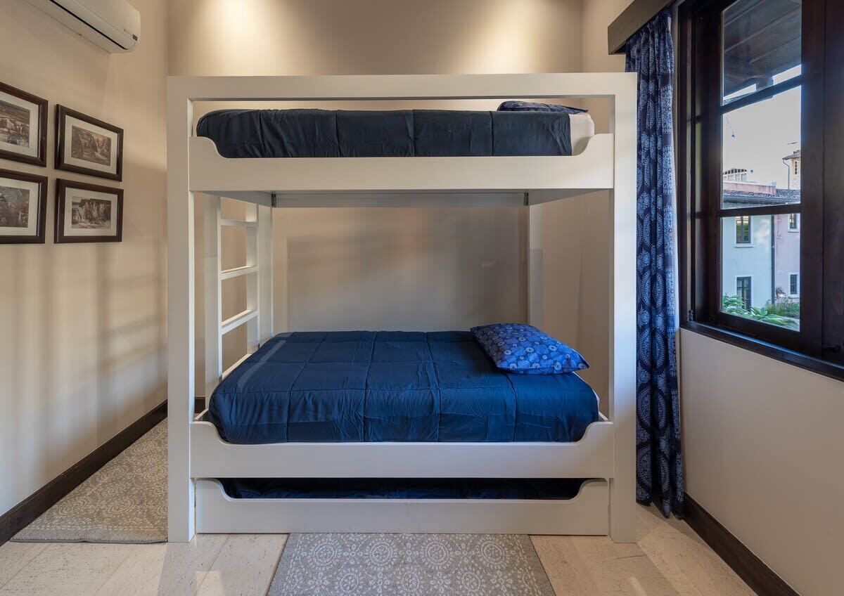 A bunk bed room with a window, a patterned rug, and framed pictures on the wall.