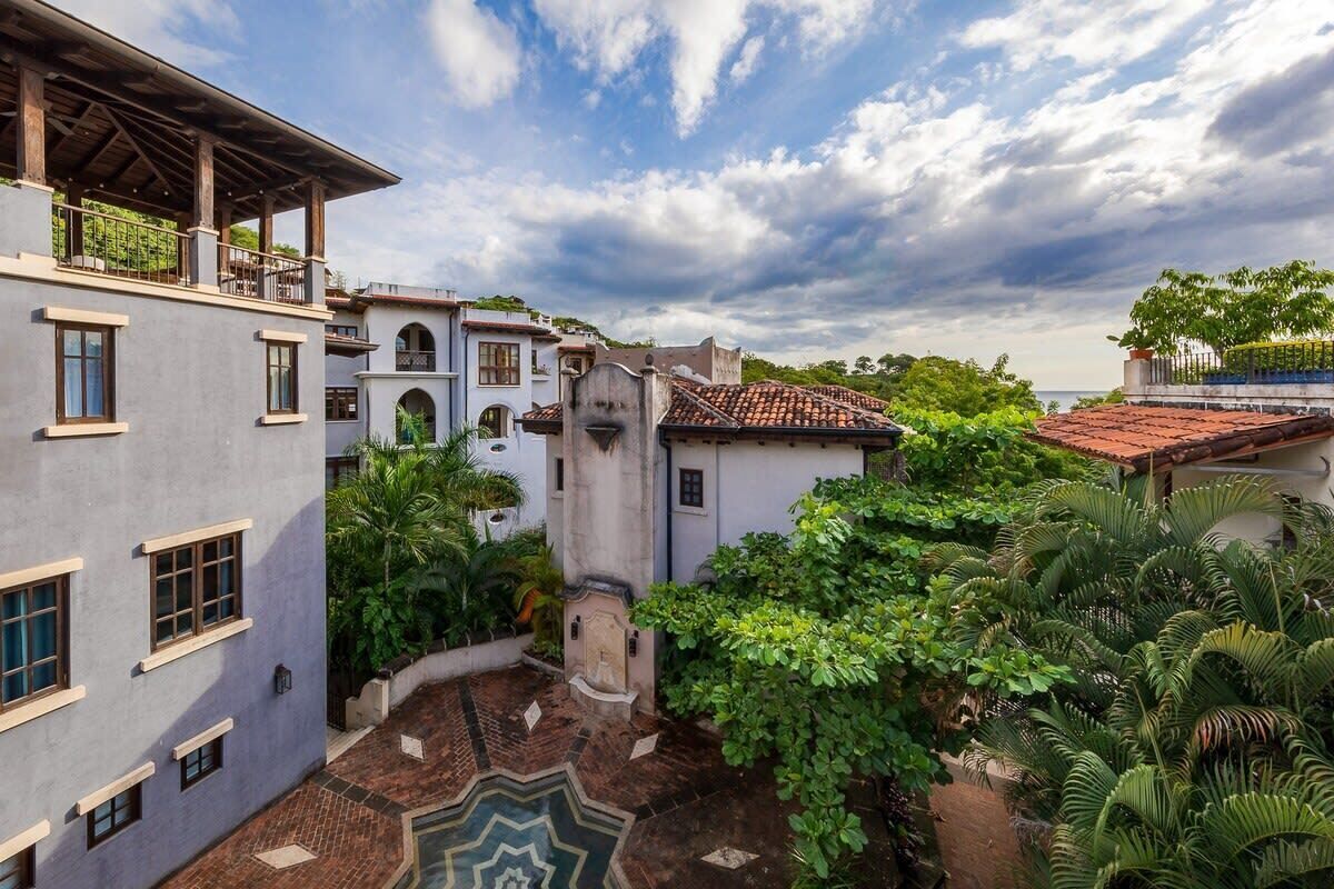 A courtyard with a pool, surrounded by buildings with a mix of modern and traditional architecture, including a balcony and a covered area.