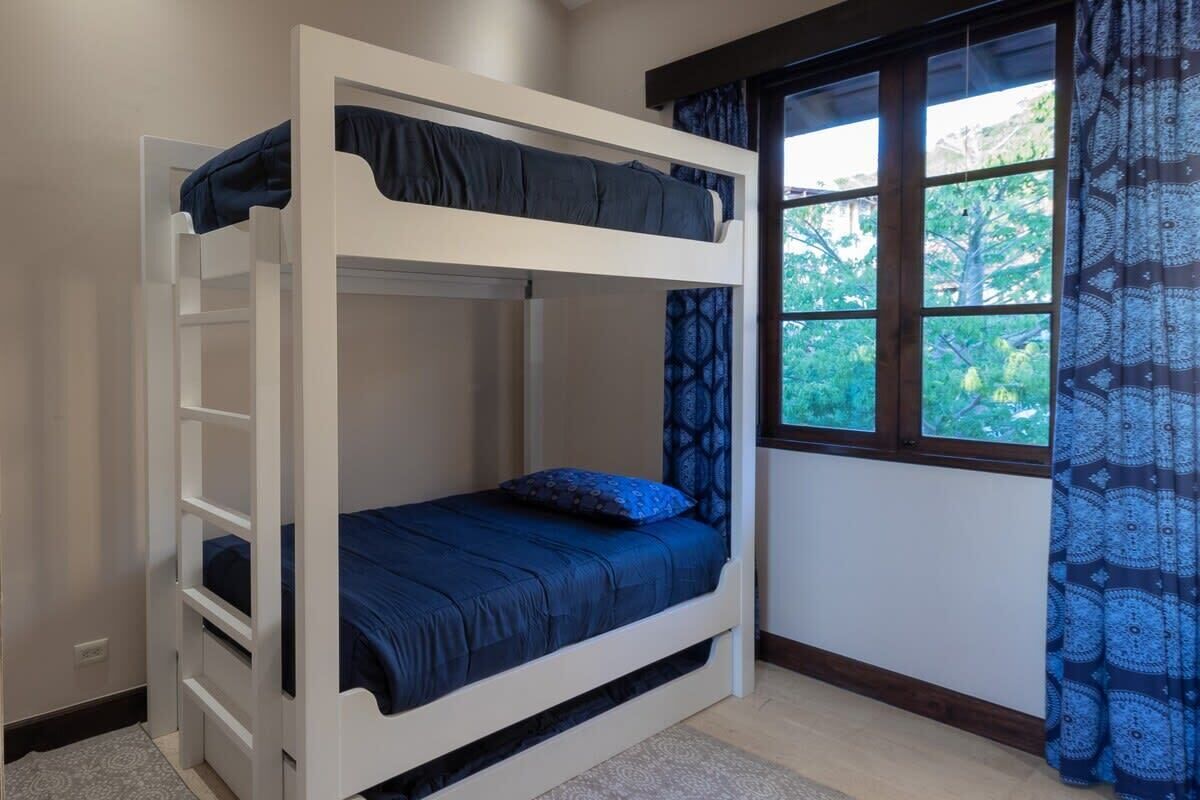 Een stapelbed met een onderbed, een raam met behang en uitzicht op groen.