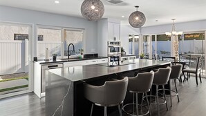Una cucina moderna con una grande isola, sgabelli da bar, illuminazione a sospensione e vista sul giardino.