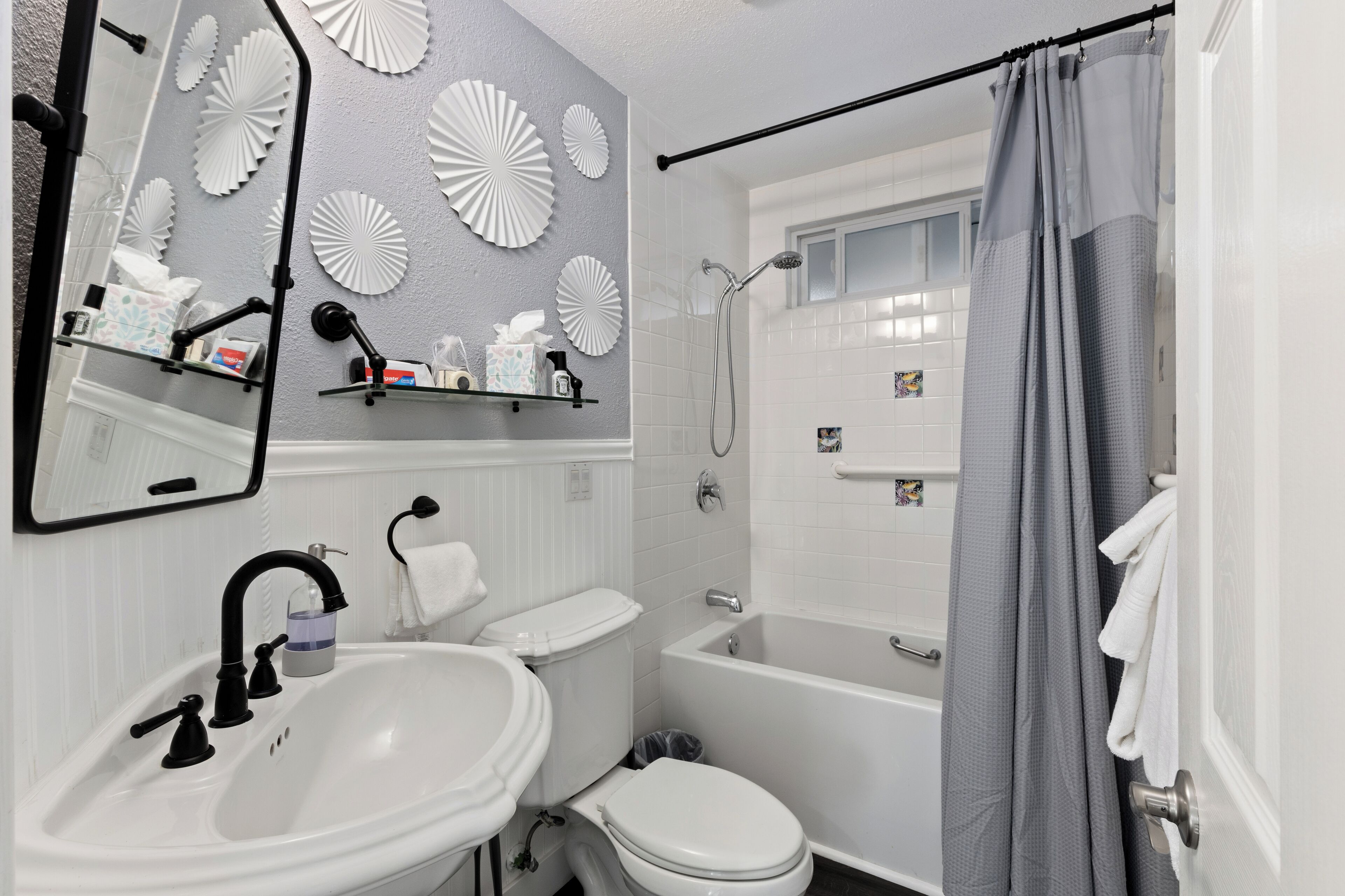 Une salle de bain avec un lavabo, des toilettes et une baignoire. On y trouve des éléments décoratifs fixés au mur et un rideau de douche.