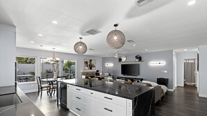 Una cucina moderna con isola centrale, zona pranzo con sedie, un lampadario e una TV nella zona living.