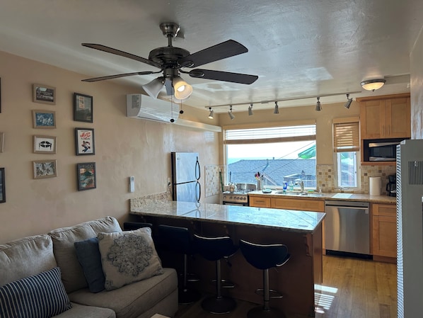 A kitchen with a ceiling fan, bar stools, a refrigerator, a stove, and a window with blinds.