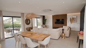 A modern living room with a wooden dining table, white sofas, and a large TV. - AZUR -  NEW SEA SIDE DR, 4 BR, 4.5 BA -  WALK TO  INDIGO BEACH (Sint Maarten)