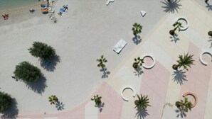 An aerial view of a beach area with palm trees, sun loungers, and a tiled walkway. - Seaside Apartment with Pool (Split)