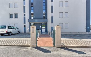 Un bâtiment moderne doté d’une entrée sécurisée par un portail, un fourgon blanc garé à l’extérieur et une zone pavée avec des places de stationnement numérotées.