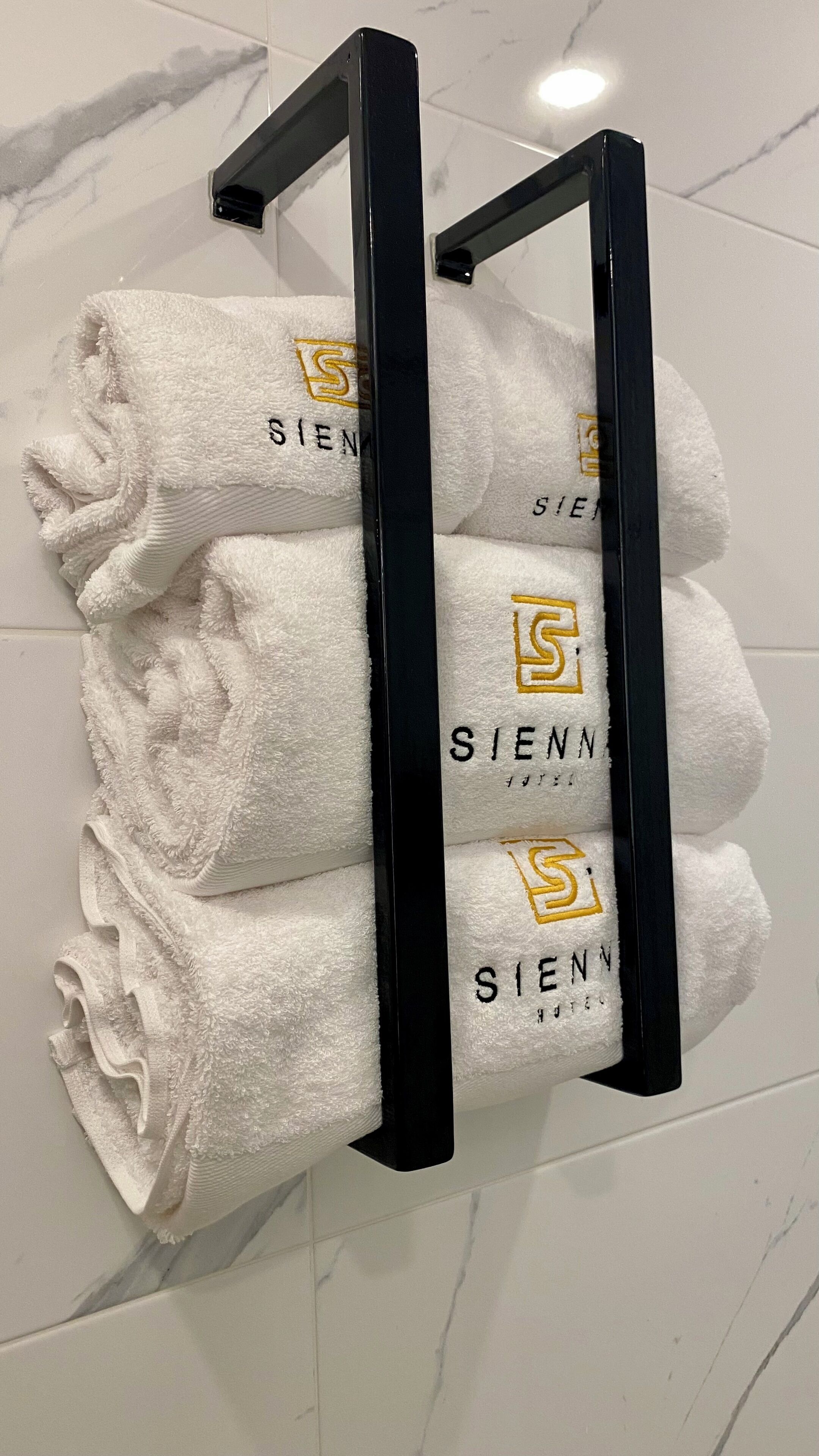 A towel rack with four white towels, each with a logo and the word "SIENN" printed on them.