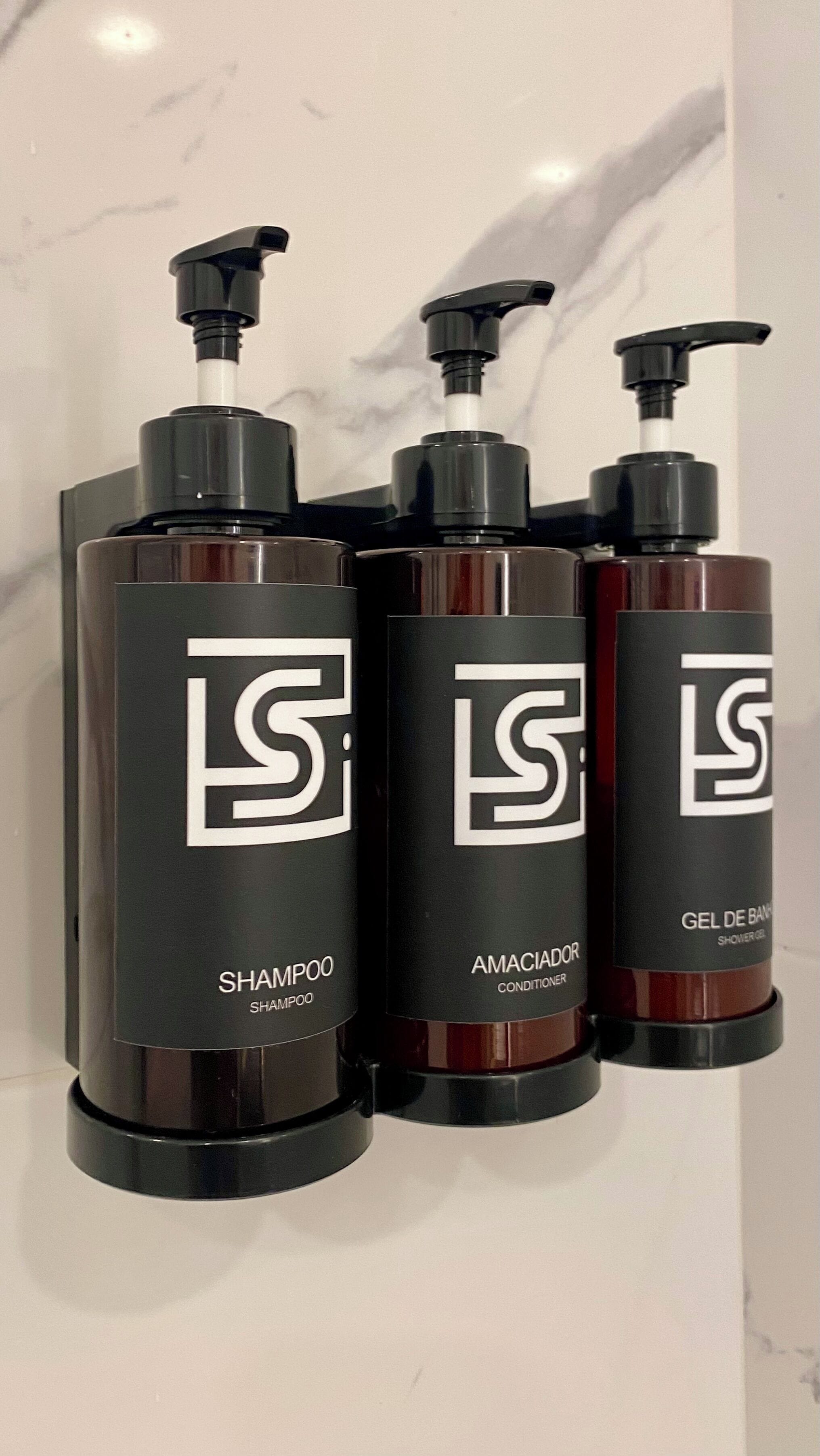 Three bottles of shampoo, conditioner, and shower gel with pumps, arranged on a white surface.