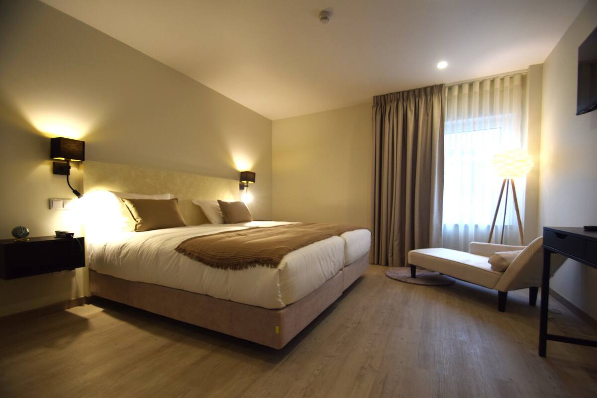 A modern hotel room with a large bed, bedside lamps, a desk, and a view of the outdoors.