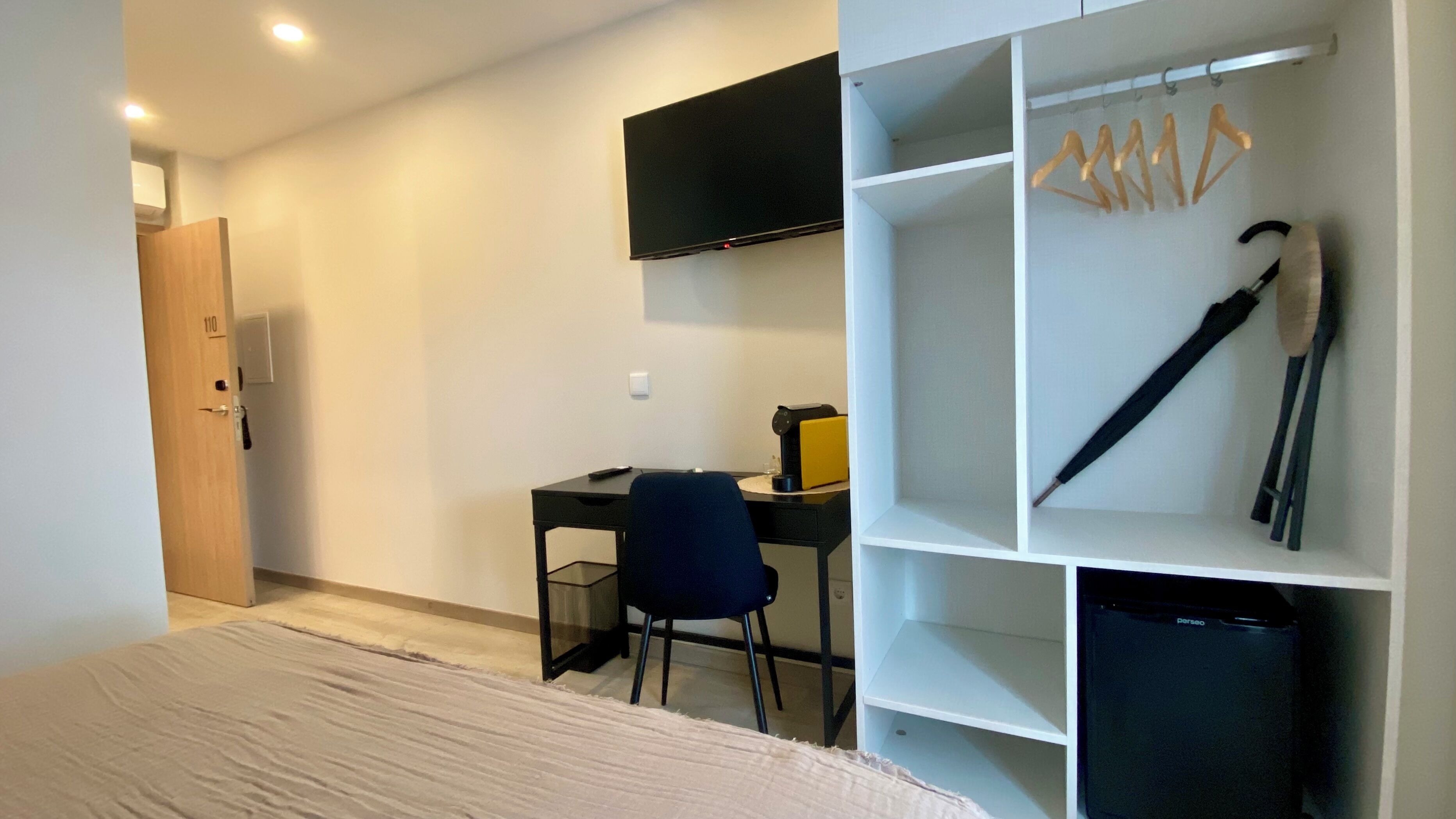 Een slaapkamer met een bed, een bureau, een stoel, een televisie en een kledingkast met kledinghangers.