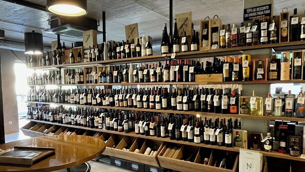 A wine store with shelves stocked with various bottles of wine, wooden display cases, and a counter with a wine barrel. - SIENNA Hotel (Rio Maior)