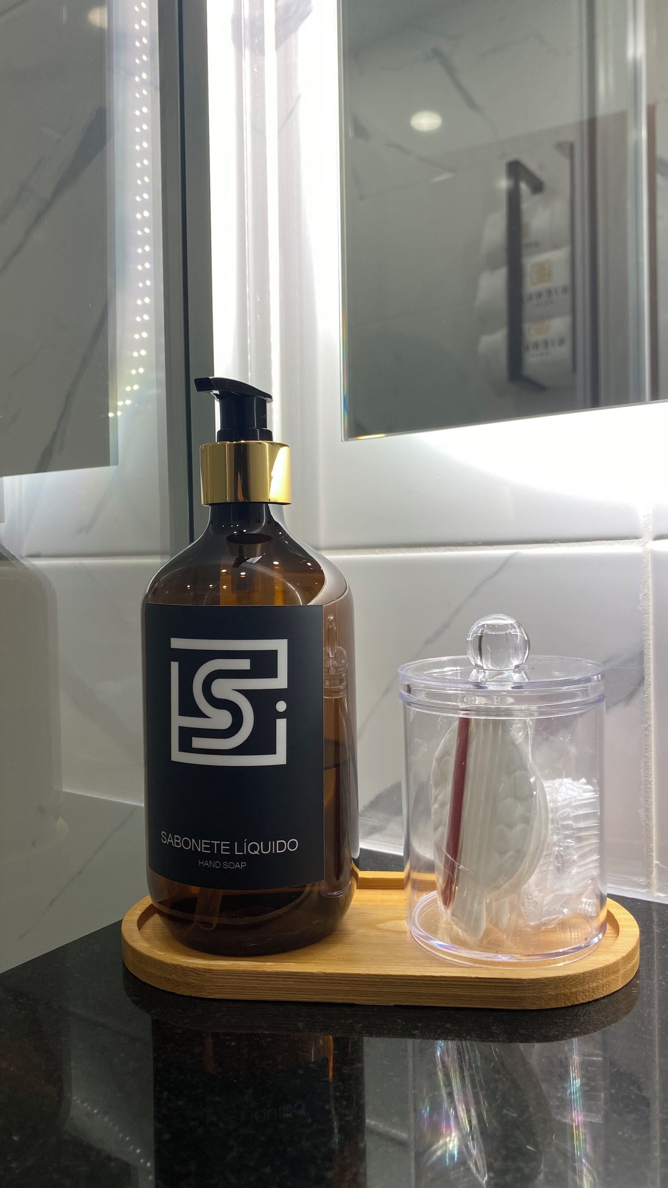 A bottle of hand soap and a glass container on a wooden tray.