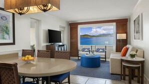 Un salon moderne comprenant un coin repas, un téléviseur et une grande fenêtre donnant sur la mer.