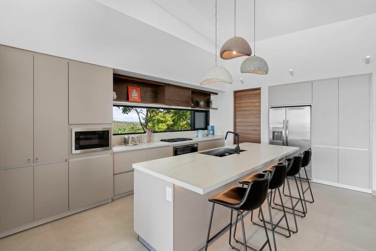 A modern kitchen with a central island, bar stools, built-in appliances, and pendant lighting.