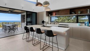 A modern kitchen with a large island, bar stools, and a view of the ocean. - Luxurious Ultramodern Property with Private Suites, Infinity Pool, and Sweeping Ocean and Mountain Views (Sardinal)