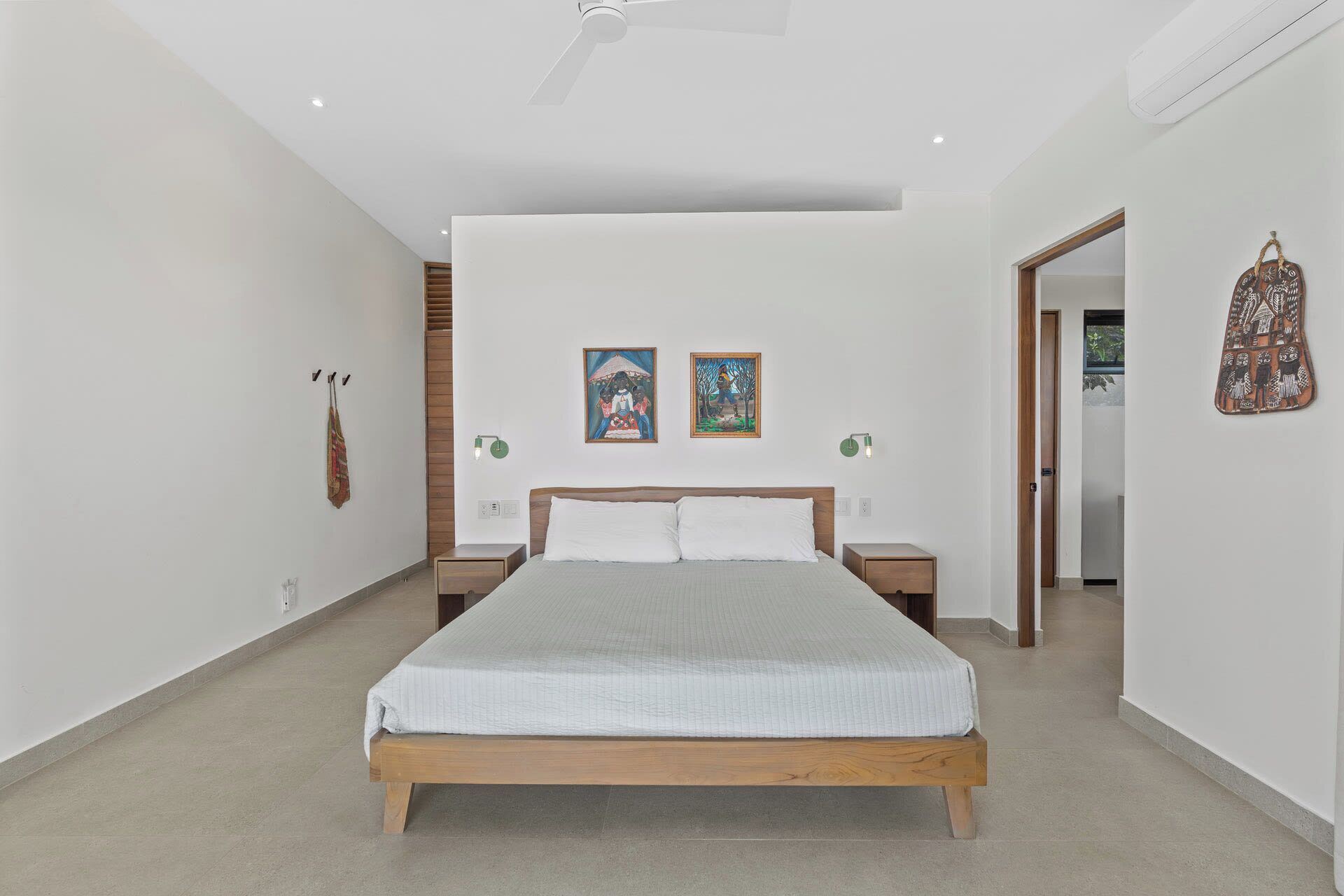 A modern bedroom with a wooden bed, two wall-mounted paintings, and a hanging bag.