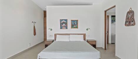 A modern bedroom with a wooden bed, two wall-mounted paintings, and a hanging bag.