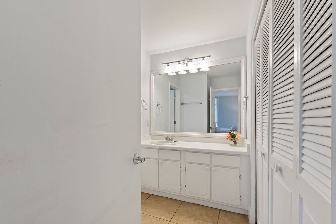 Un baño con un tocador blanco, un espejo grande con iluminación y una puerta con vidrio ranurado.