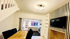 A modern kitchen with a built-in stove, a dining area with a wooden table and black chairs, and a TV mounted on a wooden panel. - Modern 2-bed house  in Blyth centre  with two bedrooms and two bathrooms (Blyth)