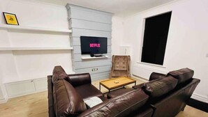 A living room with a brown leather sofa, a coffee table, and a flat-screen TV mounted on a light grey wall. - Modern 2-bed house  in Blyth centre  with two bedrooms and two bathrooms (Blyth)