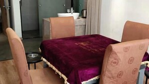 A room with a table covered by a dark red cloth, four chairs with patterned upholstery, a white sink, and a mirror above the sink. - Biligong Hotel Shanghai (Shanghai)