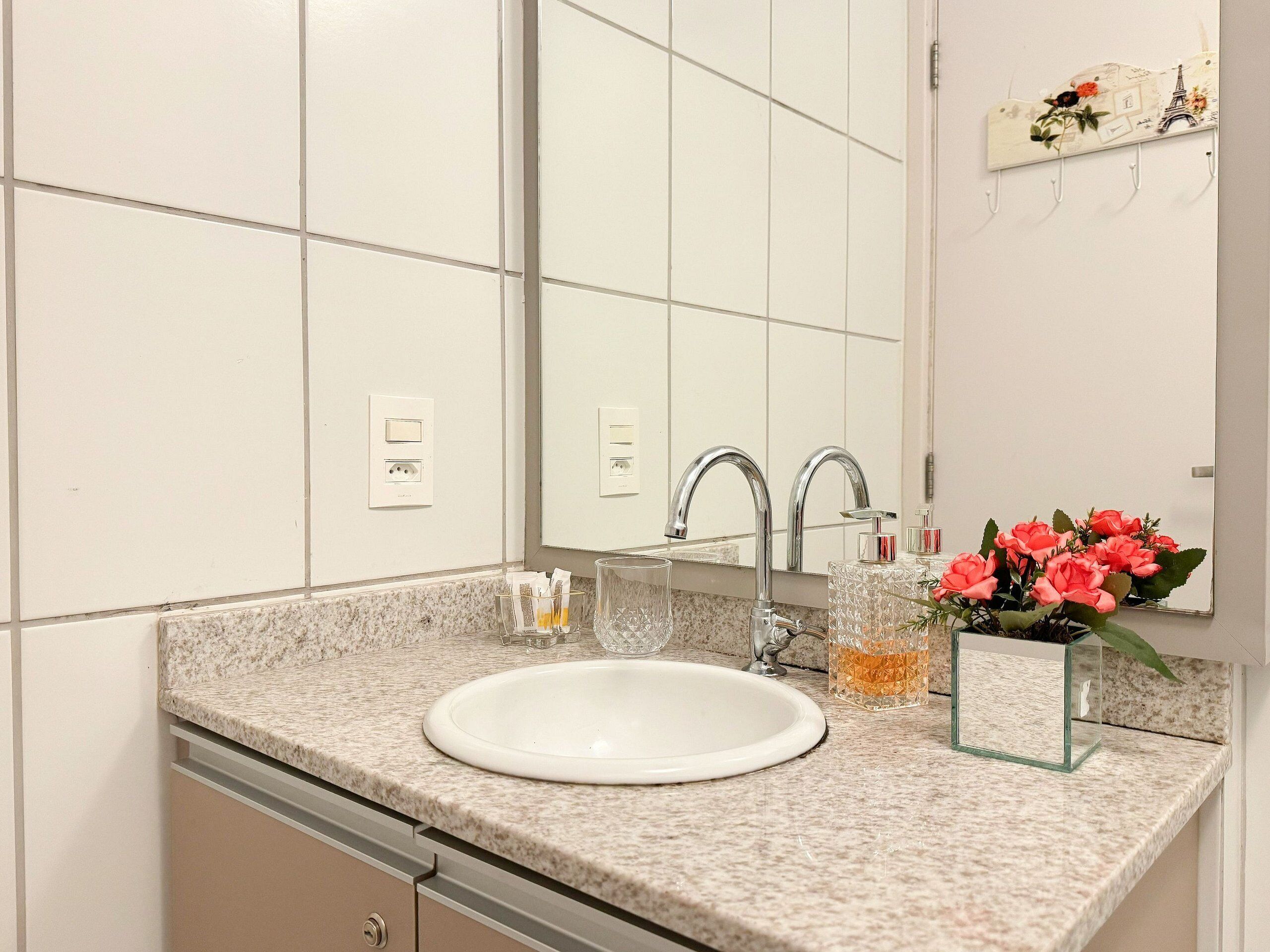 Een badkamer met een witte wastafel, twee kraanwerk, een spiegel en een decoratief object met bloemen.