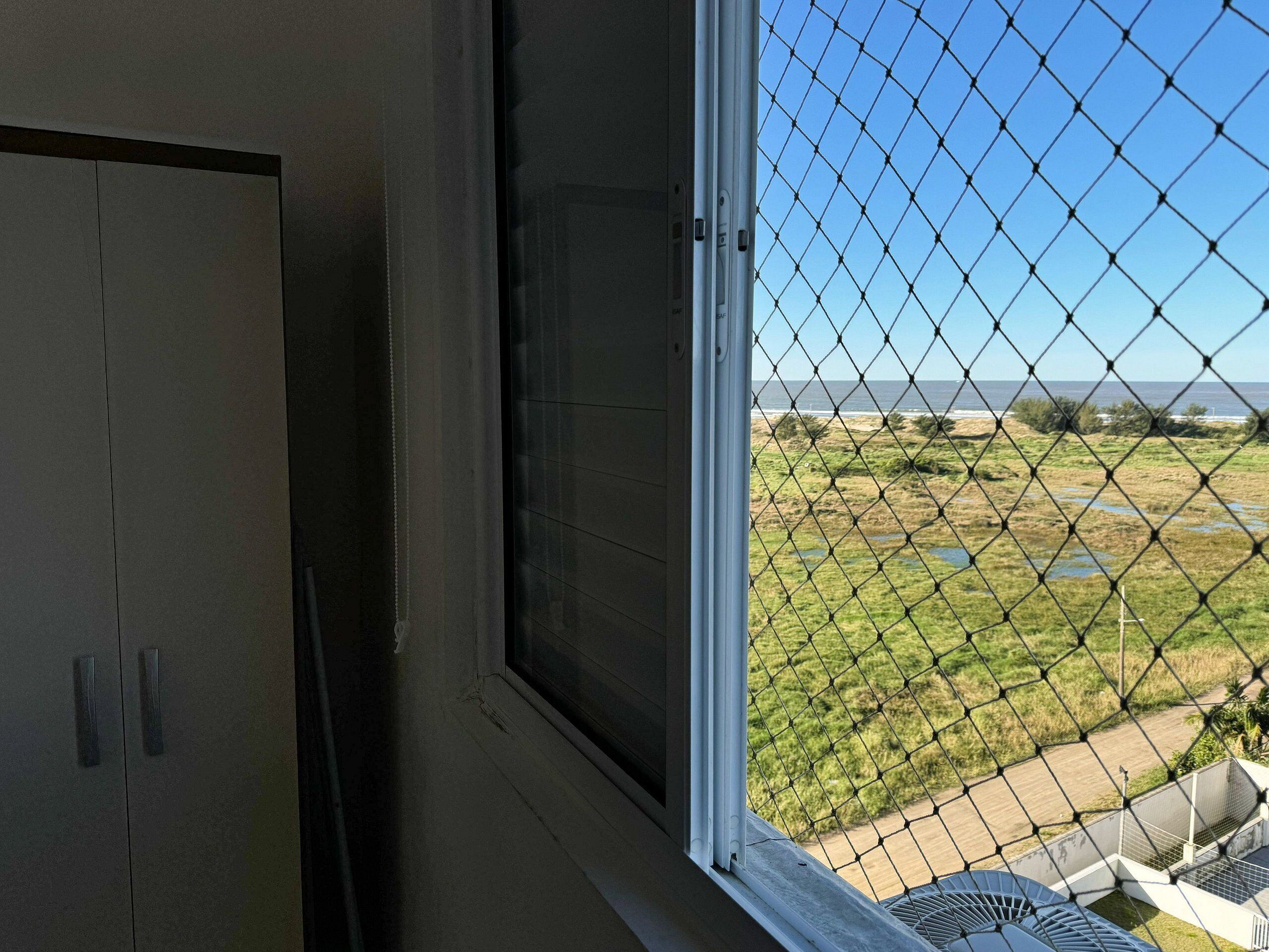 Quarto com janela vista para uma área gramada e um corpo d'água.