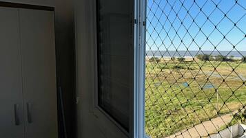 Quarto com janela vista para uma área gramada e um corpo d'água.