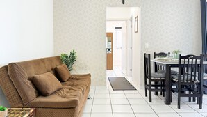 Ein Wohnzimmer mit braunem Sofa, einem Glastisch und einem Essbereich mit Tisch und Stühlen.