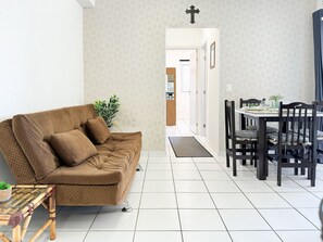 Een woonkamer met een bruine bank, een glazen salontafel en een eethoek met een tafel en stoelen.