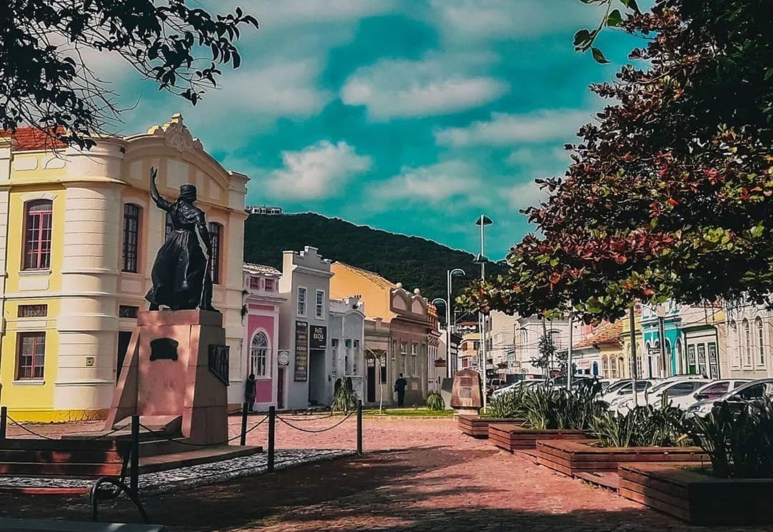 A street with a statue, buildings, and parked cars.