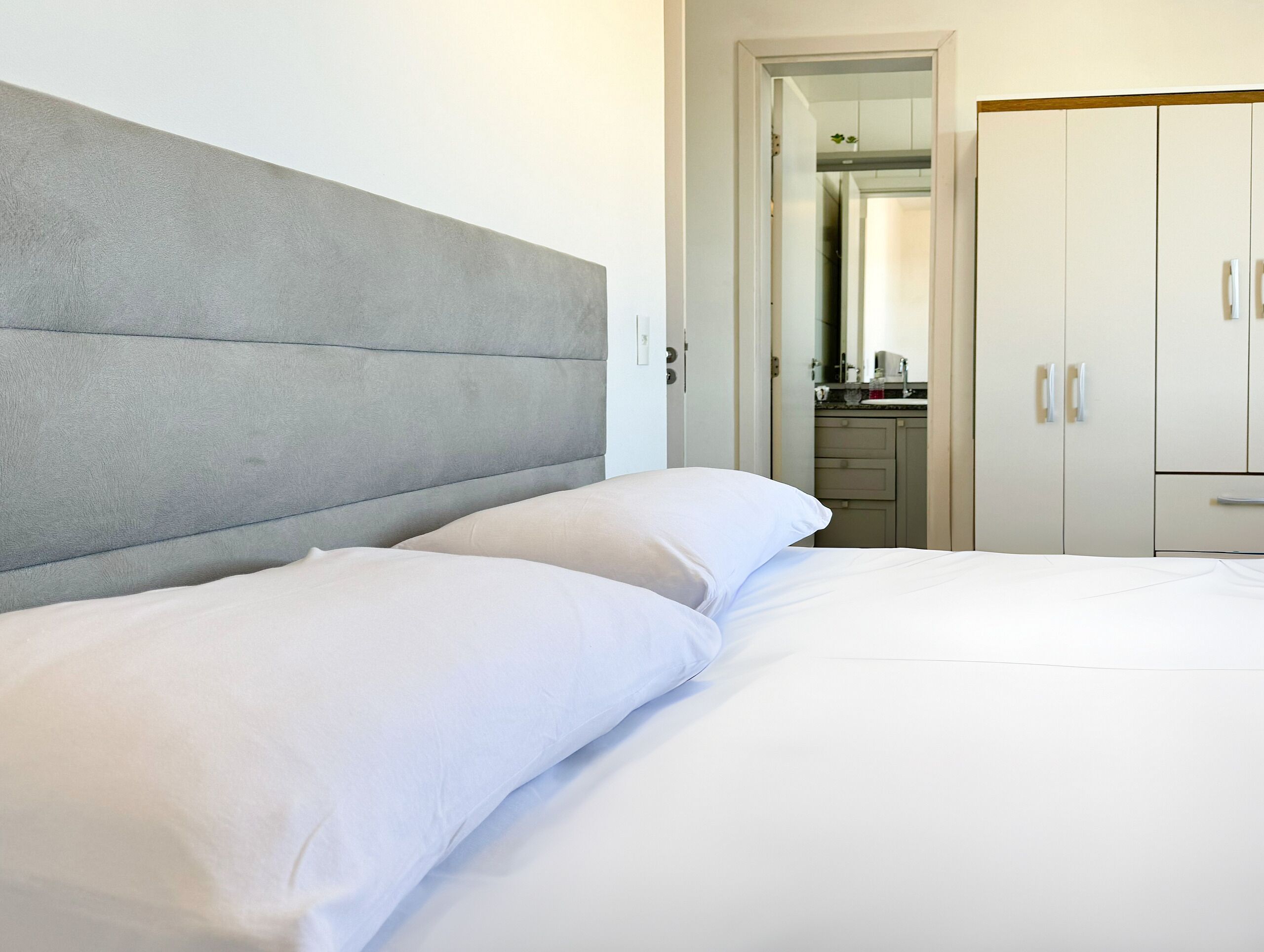 A hotel room with a large bed, a grey headboard, and a wardrobe with two doors.