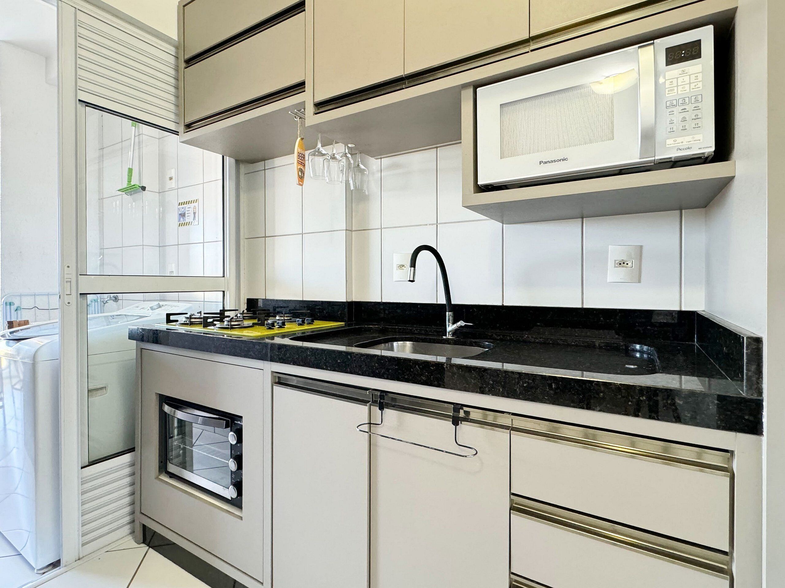 Una cocina moderna con armarios blancos, encimera negra, horno empotrado, microondas y un lavabo.